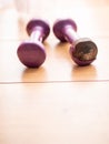 Two light small purple color dumbbell on a wooden floor. One has serious damage to plastic surface. Hard fitness workout concept.