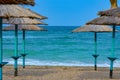 Two lines of straw beach umbrellas providing shade near the wavy water of the Black Sea on sandy shoreline on a sunny clear summer