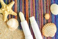 Two lip balms, sunscreen sticks on the colorful beach towel wirh sand and seashells. Summer lip treatment and UV protection