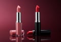 Two lipsticks displayed with caps and applicators on reflective surface Royalty Free Stock Photo