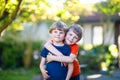 Two little active school kids boys, twins and siblings hugging on summer day