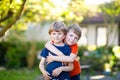 Two little active school kids boys, twins and siblings hugging on summer day