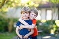 Two little active school kids boys, twins and siblings hugging on summer day