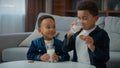 Two little African American boys kids ethnic adopted hungry children drink milk eat cookies at home living room siblings Royalty Free Stock Photo