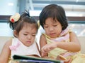 Two little Asian baby girl, sisters, sitting and watching a smartphone together, while waiting for her mother