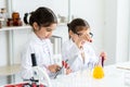 Two little Asian girls in white lab coat help each other for experiment. Little glasses girl using pipette drop solution in yellow Royalty Free Stock Photo