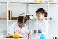 Two little Asian girls in white lab coat help each other for experiment. Little glasses girl writing her new idea by pencil for Royalty Free Stock Photo