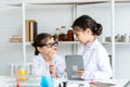 Two little Asian girls in white lab coat help each other for experiment. Little glasses girl showing violet solution inside Royalty Free Stock Photo