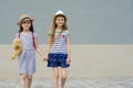 Two little beautiful girlfriends holding hands, girls walking in striped dresses, hats with backpack