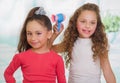Two little beautiful girls posing for camera, curly girl is holding a hair dryer and brunette is wearing a red blouse Royalty Free Stock Photo