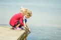 Two little blonde kids, boy and girl, sitting on a pier on a lake or river and searching for something or fishing with wooden Royalty Free Stock Photo