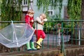 Two little boys, best friends and siblings walking with big umbrella outdoors on rainy day. Preschool children having