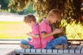 Two little boys playing games on mobile phone in sunny day, sitting back to back. Royalty Free Stock Photo