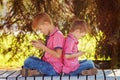 Two little boys playing games on mobile phone in sunny day, sitting back to back. Royalty Free Stock Photo