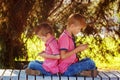 Two little boys playing games on mobile phone in sunny day, sitting back to back. Royalty Free Stock Photo