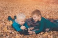 Two little brothers look at pictures on the camera. Lying in yellow autumn leaves. Fall day