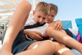 Two little caucasian blond little child boys enjoy having fun using smartphone sitting on lounger at beach summer Royalty Free Stock Photo