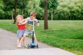 Two little Caucasian preschool children fighting in park outside. Boy and girl can not share one scooter.