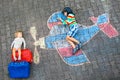 Two little children, kid boy and toddler girl having fun with with airplane picture drawing with colorful chalks on