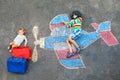 Two little children, kid boy and toddler girl having fun with with airplane picture drawing with colorful chalks on Royalty Free Stock Photo