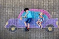 Two little children, kid boy and toddler girl having fun with with car picture drawing with colorful chalks on asphalt