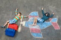 Two little children, kids boys having fun with with airplane picture drawing with colorful chalks on asphalt. Friends