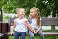 Two little children laugh and chat on a bench. Girls with backpacks. The concept is back to school, family and childhood