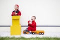 Two little courier boys in red uniform with yellow cardboard boxes and large toy car on light background Royalty Free Stock Photo