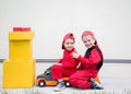 Two little courier boys in red uniforms are sitting on a large toy car with yellow cardboard boxes on a light background Royalty Free Stock Photo