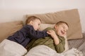 Two little and cute caucasian boys playing together on the bed at home. Interior and clothes in natural earth colors