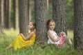 Two little cute girls sitting near the tree in a pine forest. Summer. Royalty Free Stock Photo