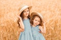 Two little cute girls in a straw hat and a blue dress among a golden wheat field. sisters holding hands Royalty Free Stock Photo