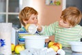 Two little funny brothers baking apple cake in domestic kitchen. Happy healthy kid boys having fun with working with Royalty Free Stock Photo