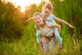 Two little funny sister playing outside on sunset. Little girl climbed up on back of cute sister and fly