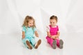 Two little girlfriends in the identical overalls of different colors sitting on the floor in a studio with white walls