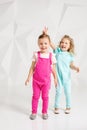 Two little girlfriends in the identical overalls of different colors in a studio with white walls