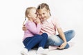 Two little girlfriends in jeans and pink sweaters gossip. White background