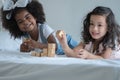 Two little girls, African and Asian children enjoy playing build wooden block together on bed Royalty Free Stock Photo
