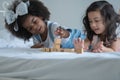 Two little girls, African and Asian children enjoy playing build wooden block together on bed Royalty Free Stock Photo