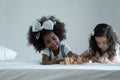 Two little girls, African and Asian kids enjoy playing build wooden block together on bed at bedroom Royalty Free Stock Photo