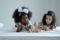 Two little girls, African and Asian kids enjoy playing build wooden block together on bed at bedroom Royalty Free Stock Photo