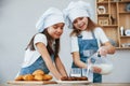 Two little girls in blue chef uniform pouring milk into glasses on the kitchen with cookies on table Royalty Free Stock Photo
