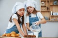 Two little girls in blue chef uniform pouring milk into glasses on the kitchen with cookies on table Royalty Free Stock Photo
