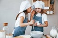 Two little girls in blue chef uniform talking secrets to each other when preparing food on the kitchen