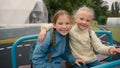 Two little girls friends sisters riding swing laughing smiling joy happiness childhood playground hug fun schoolgirls Royalty Free Stock Photo