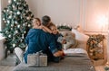 two little girls hug their daddy sitting on the bed near the Christmas tree. children's happiness and joy
