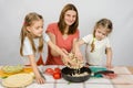 Two little girls at kitchen table with a zeal to help her mother pour the mushrooms from the plate to the pan