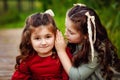 Two little girls with long hair in a red and green dress are sitting, playing and having fun in the Park on the path. Two happy