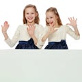 Two little girls peeking out from behind a white advertising ban Royalty Free Stock Photo