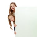 Two little girls peeking out from behind a white advertising ban Royalty Free Stock Photo